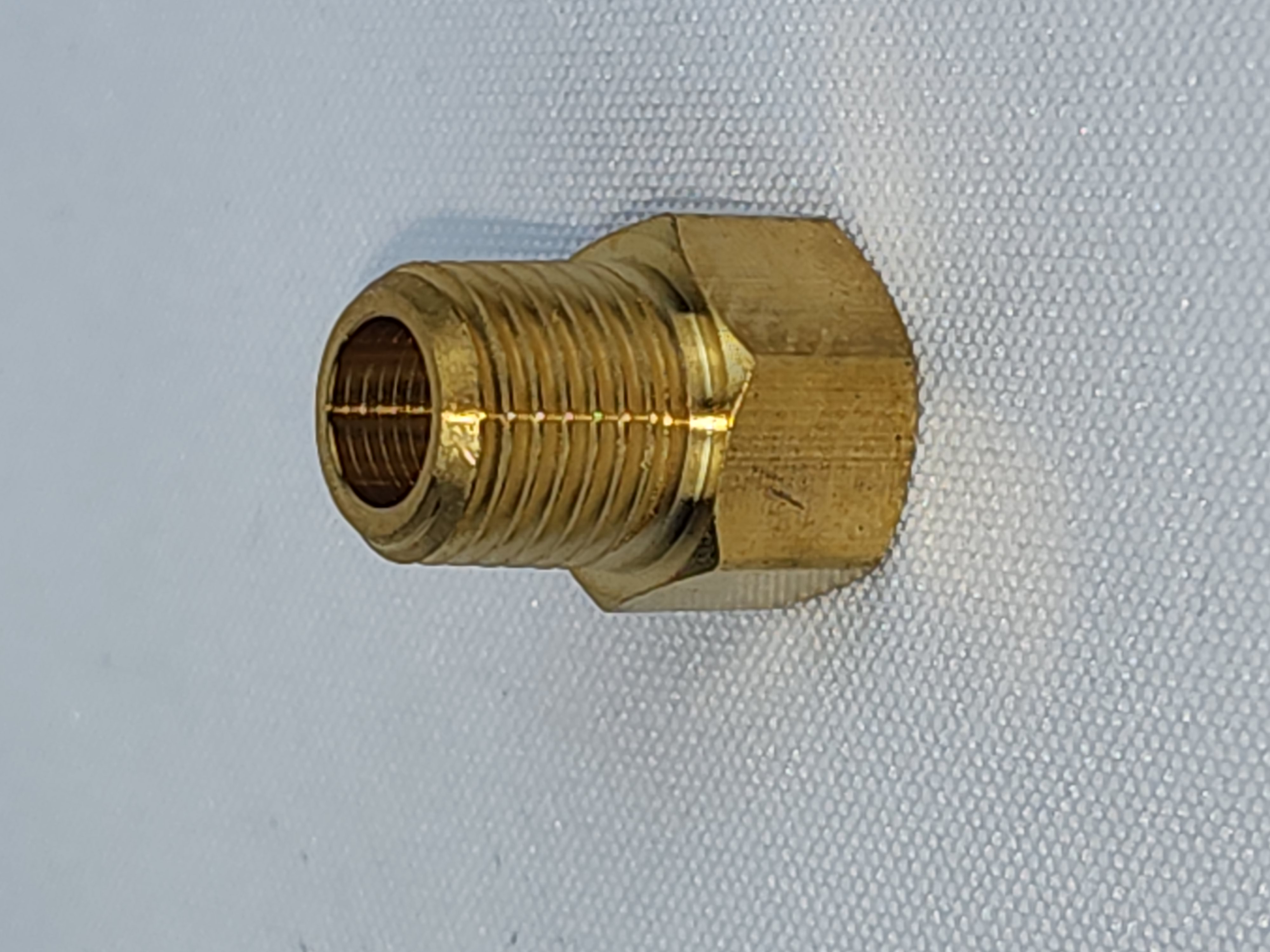 A brass pipe fitting sitting on top of a white surface.